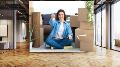 Moving to a new house, rental housing. Happy young caucasian woman sitting on the floor with cardboard boxes in her new home and holding keys, friendly smiling happy looking at the camera Wall mural