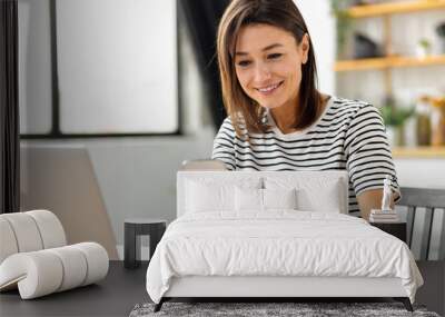 Online shopping, technology concept. Happy Caucasian woman holding mobile phone and credit card sitting at the table in the home kitchen Wall mural