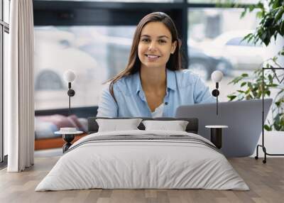 Portrait of successful female freelancer or employee sitting at workplace, co-working. Smiling caucasian woman using laptop computer, working at modern office or home smiling and looking at the camera Wall mural