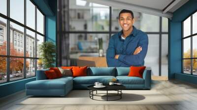 Portrait of successful young african american businessman with arms crossed standing in modern office. Happy entrepreneur looking at the camera and smiling friendly Wall mural