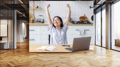 Relaxed young Asian woman freelancer or student stretching hands and body taking break happy with task done at workplace in home, smiling Wall mural