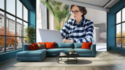 Serious elderly woman working laptop. Business woman busy working on laptop at home office Wall mural