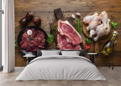 Various meat, beef steak, chicken legs and liver with cooking ingredients on wooden table top view Wall mural