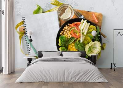 Vegan healthy balanced diet. Vegetarian buddha bowl with blank notebook and measuring tape. Сhickpeas, broccoli, pepper, tomato, spinach, arugula and avocado in plate on white background Wall mural