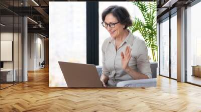 Video call, remote work concept. Beautiful caucasian aged business woman using laptop computer for online communication via the internet sitting on an armchair in the office or at home Wall mural