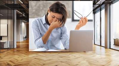 Young caucasian woman businessman feel eye strain holding glasses, rubbing the bridge of her nose. Female tired from long work at the computer sitting at the desk in the office Wall mural