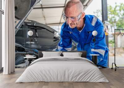 A male auto mechanic in blue jumpsuit writing engine repair notes on his paper notepad while working its engine at car repair garage Wall mural