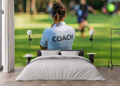 back view of a female sport coach watching her team compete at an outdoor football field Wall mural