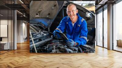 Happy car mechanic holding a computer tabet and smiling at camera while working at car's engine Wall mural