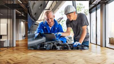 Two auto mechanics using a computer tablet while working together on the car engine at car repair garage Wall mural