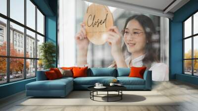 Young female shop owner holding the Closed sign that hanging on the shop glass window Wall mural