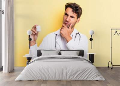 hispanic handsome man thinking, feeling doubtful and confused. physician bottle pills concept Wall mural