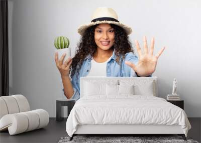 hispanic pretty woman smiling and looking friendly, showing number five wearing a hat and holding a houseplant Wall mural