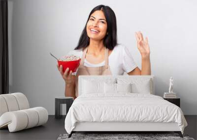 pretty hispanic woman pretty hispanic chef woman smiling happily, waving hand, welcoming and greeting you and holding a corn flakes bowl Wall mural