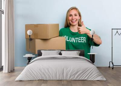 young adult blonde woman feeling proud,smiling positively with thumbs up. volunteer and donation concept Wall mural