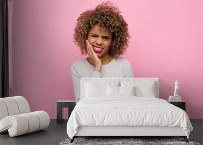 young african american woman holding cheek and suffering painful toothache, feeling ill, miserable and unhappy, looking for a dentist against pink wall Wall mural