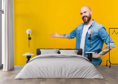 young bald and bearded man feeling happy and cheerful, smiling and welcoming you, inviting you in with a friendly gesture Wall mural