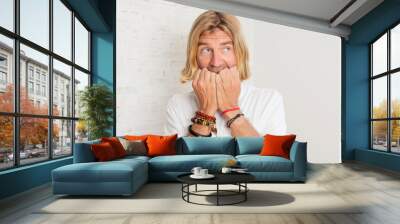 young blond adult man looking worried, anxious, stressed and afraid, biting fingernails and looking to lateral copy space Wall mural