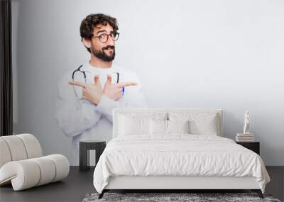 young doctor man looking puzzled and confused, insecure and pointing in opposite directions with doubts against copy space wall Wall mural