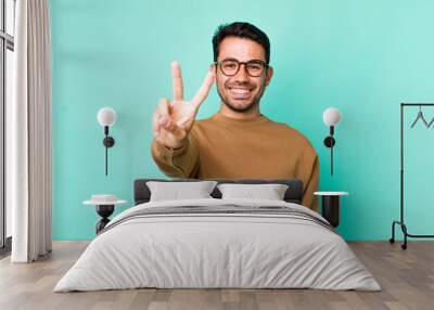 young handsome hicpanic man smiling and looking friendly, showing number two or second with hand forward, counting down Wall mural