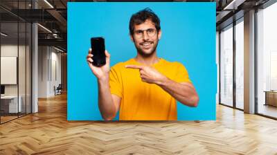 young handsome indian man pointing or showing and holding a mobile telephone Wall mural