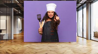 young hispanic woman pointing at camera with a satisfied, confident, friendly smile, choosing you. barbecue chef concept Wall mural