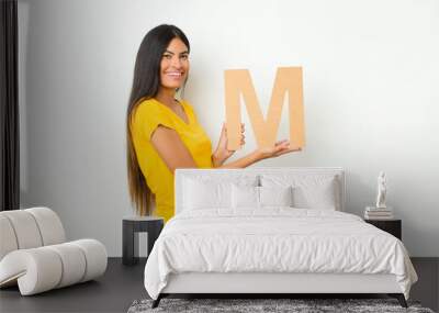 young latin pretty woman excited, happy, joyful, holding the letter M of the alphabet to form a word or a sentence. Wall mural