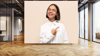 young latin woman looking excited and surprised pointing to the side and upwards to copy space Wall mural