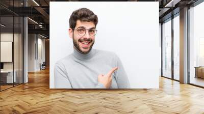 young manager man looking excited and surprised pointing to the side and upwards to copy space against white wall Wall mural