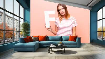 young pretty red head woman angry, anger, disagreement, holding the letter F of the alphabet to form a word or a sentence. Wall mural