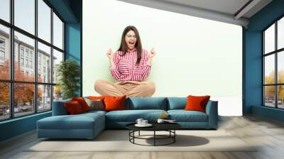 young pretty woman looking extremely happy and surprised, celebrating success, shouting and jumping sitting on the floor Wall mural