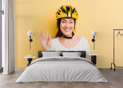 young pretty woman smiling happily, waving hand, welcoming and greeting you. bike helmet concept Wall mural