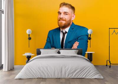 young red head businessman shrugging, feeling confused and uncertain, doubting with arms crossed and puzzled look against orange background Wall mural