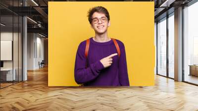 young student boy smiling cheerfully, feeling happy and pointing to the side and upwards, showing object in copy space Wall mural