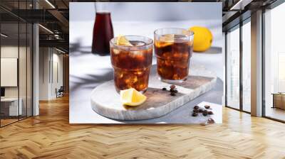 Cold brew coffee in a two glasses with lemon and ice on a marble board on a light background with coffee beans, bottle and shadows. Concept summer craft refreshing homemade drink. Wall mural