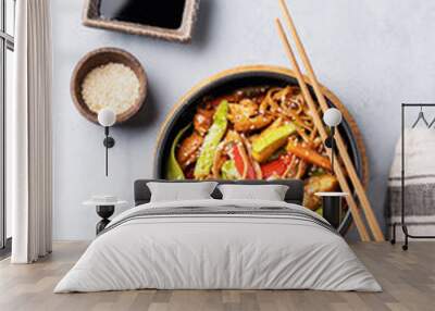 Stir-fry with soba noodles, meat and vegetables on a light background with chopsticks, soy sauce and sesame seeds. Wall mural