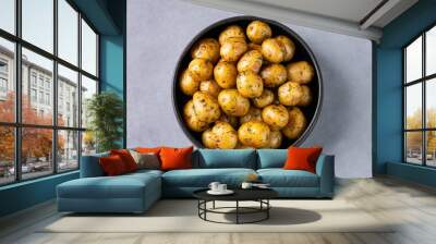 Young roasted baby potatoes in a black  pan on a blue background. Wall mural