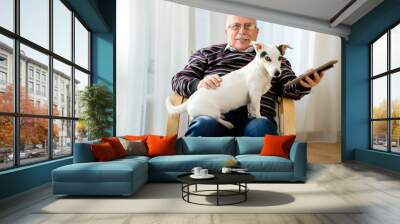 Senior man 70-75 years old sitting on armchair at home, reading, watching and relaxing tablet pc computer with his best friend, a dog Jack russell terrier. Wall mural