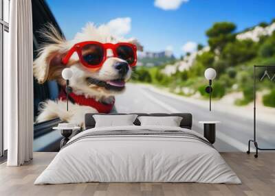 Cute dog wearing red sunglasses enjoying a car ride on a sunny day. The background shows a scenic, blurred road. Wall mural