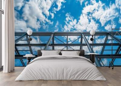 Steel structure of an industrial building against a vibrant blue sky with white clouds. Wall mural