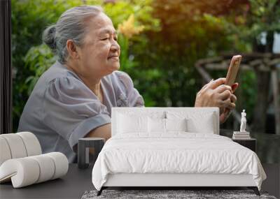 Happy old grandmother holding mobile phone, video call with loved ones while relaxing in the garden at home. Wall mural