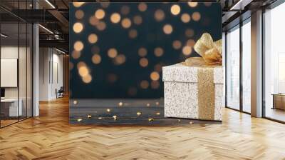 Golden Glow of Giving: A white gift box adorned with a golden ribbon sits on a dark wooden surface, illuminated by a backdrop of twinkling golden bokeh lights, evoking a sense of anticipation. Wall mural