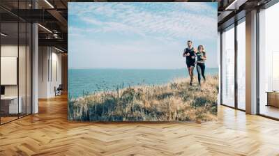 Young couple running outdoor. Male and female jogging in the countryside near the lake Wall mural