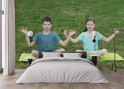 two children doing yoga sitting on a green lawn Wall mural