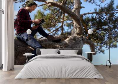 Shot of an authentic caucasian man sat on a tree branch reading a book and smiling.  Wall mural