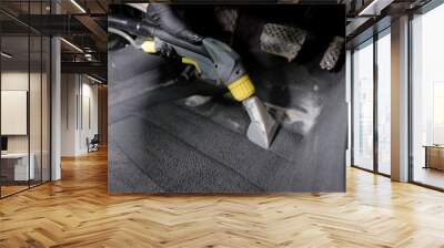 washerman is hoovering automobile carpet, cleaning by foam interior of car in a garage, wearing gloves Wall mural