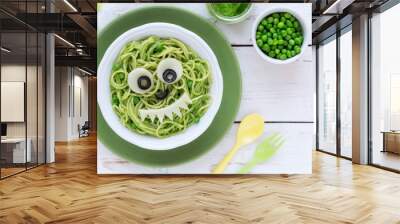 Fun food for kids - cute smiling face of green spaghetti monster served in a white bowl with eyes made of cheese and olives. Healthy vegetarian eating for children Wall mural