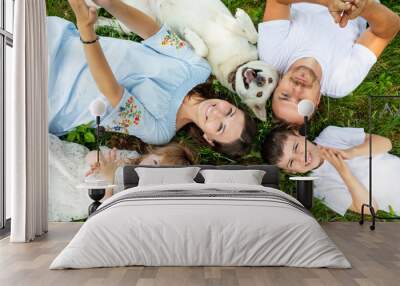 Happy beautiful big family together mother, father, children and dog lying on the grass top view Wall mural