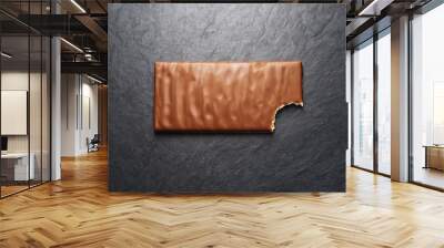 Bitten milk chocolate bar on black slate background Wall mural