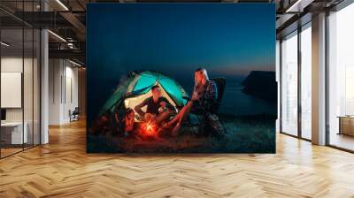 Young couple backpackers enjoying in the camping at night near the campfire. Romantic family Campsite. Happy man and woman hiking in the mountains. Wall mural